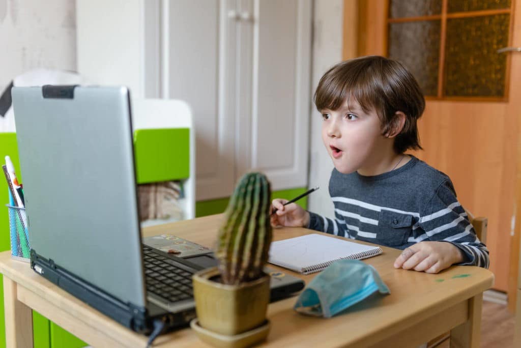 Captivated, young boy sitting at table with a notebook looking at a laptop.