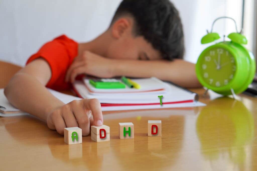 A student sits with his head down, wooden blocks sitting in front of him spelling out, “ADHD.”
