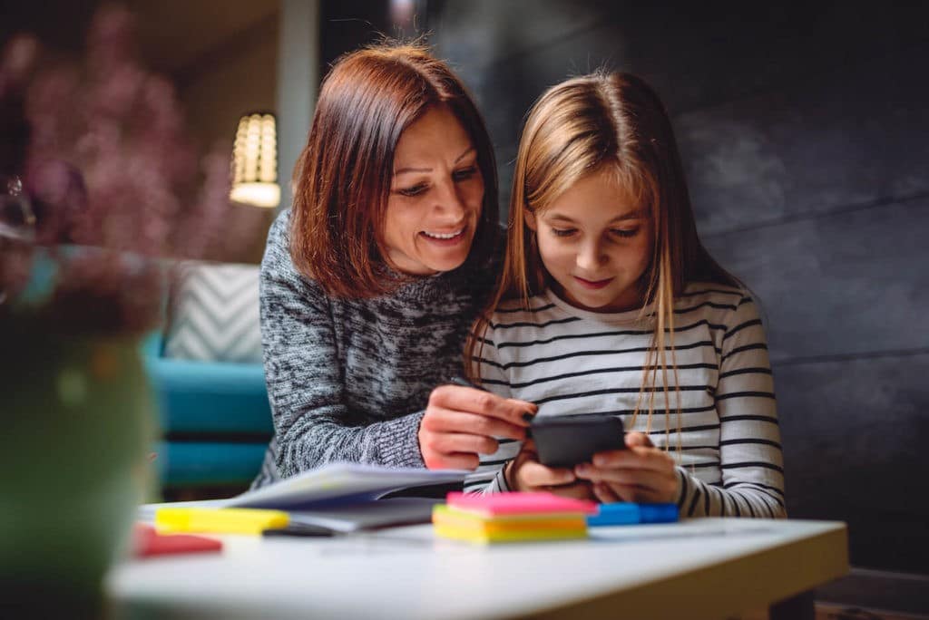 Mother and daughter do homework together while using a smart phone.