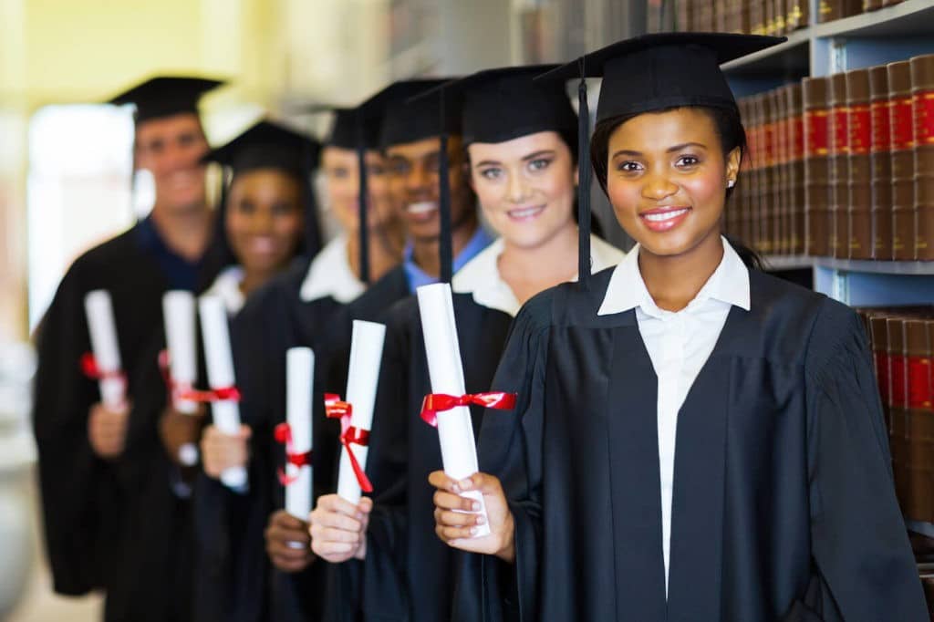 A group of graduates hold their diploma in the library.