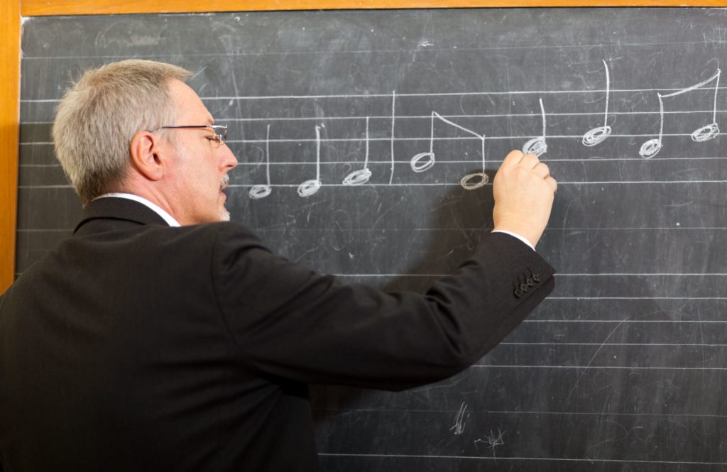 A music teacher writes words on a blackboard.