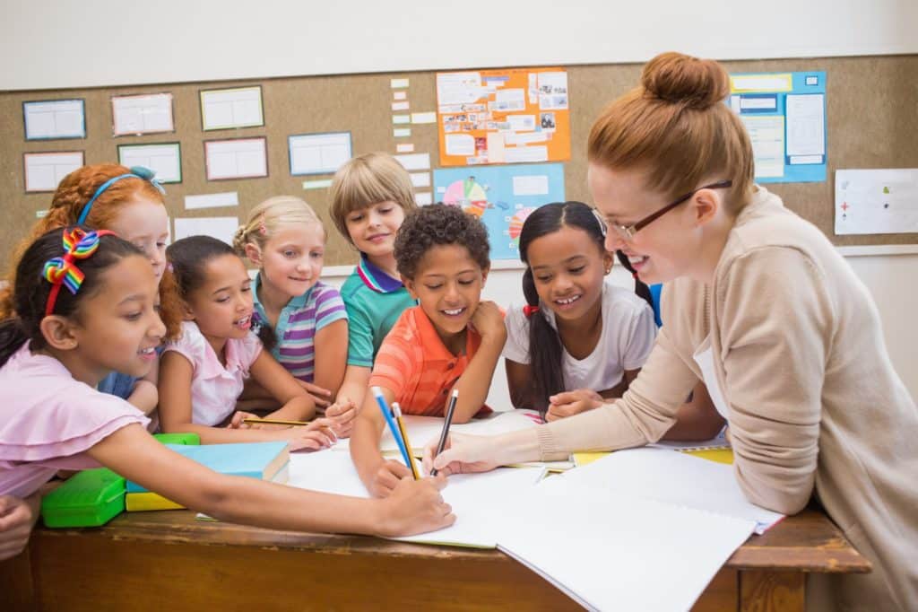 A teacher and her students smiling and working together at a table.