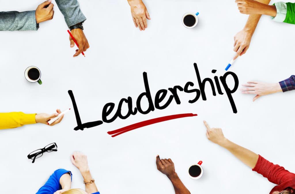 ‘Leadership’ written on a white table surrounded by reaching hands.